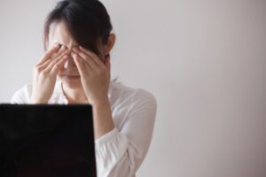 パソコンを長時間見ていて眼精疲労を感じているデスクワーカーの女性のイメージ写真